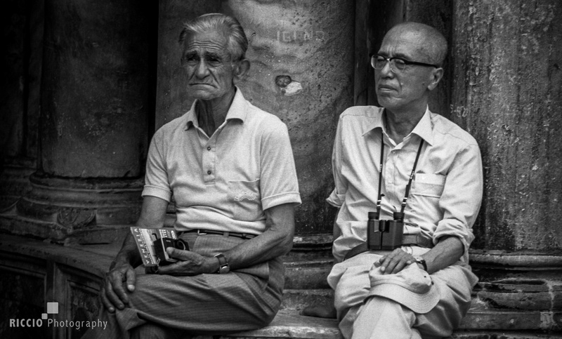 Asian and caucasian man sitting near each other in Venice. Photographed by Maurizio Riccio